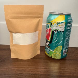 May include: A brown paper bag with a clear window next to a teal soda can. The soda can has a lime design and the text "W". The bag contains a white powder.