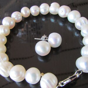 May include: A white pearl bracelet and matching stud earrings. The bracelet is strung with large, irregularly shaped pearls. The earrings feature round, lustrous pearls. The jewelry set is displayed on a reflective black surface.