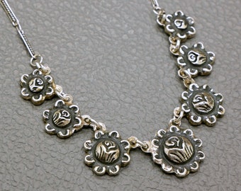 May include: A silver necklace with a delicate chain and seven silver flower-shaped pendants. Each pendant has a raised, intricate design.