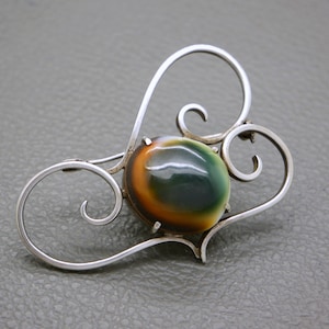 May include: A silver brooch with a swirling design and a green, brown, and orange agate stone in the center.