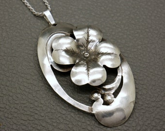 May include: A silver necklace featuring a four-leaf clover pendant. The pendant is intricately detailed with a textured design and a small bead at its centre.