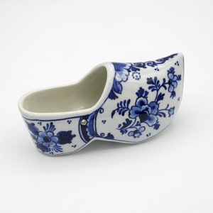 Può includere: Una scarpa olandese in ceramica blu e bianca con un motivo floreale. La scarpa è un pezzo decorativo e non è destinata ad essere indossata.