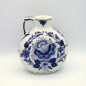 May include: A white ceramic jug with a blue and white floral design. The jug has a round body and a handle.