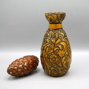 Könnte beinhalten: Eine braune und schwarze Keramikvase mit floralem Muster. Die Vase hat eine breite Öffnung und einen schmalen Hals.