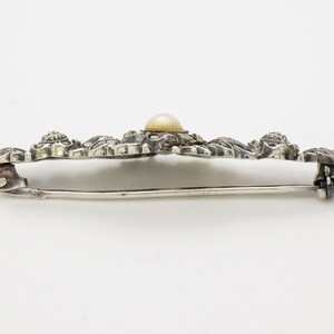 May include: A silver brooch with a delicate floral design and a single pearl in the center.