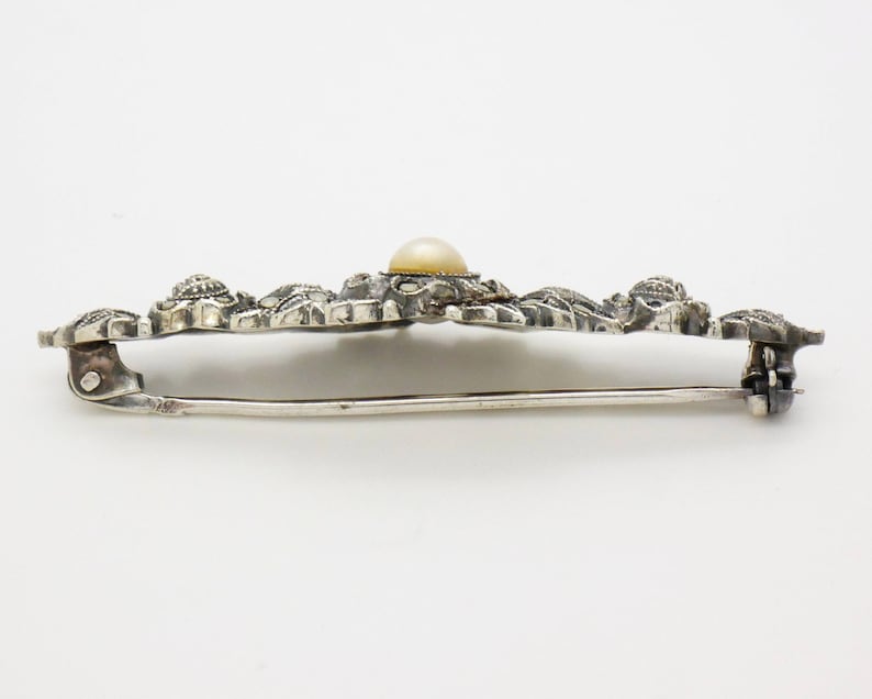 May include: A silver brooch with a delicate floral design and a single pearl in the center.