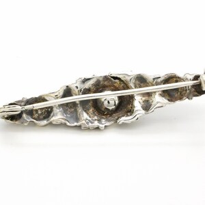 May include: A silver brooch with a detailed, organic design. The brooch is shaped like a leaf and has a textured surface. The brooch has a pin and catch closure.