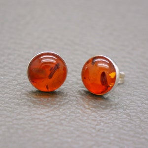 May include: A pair of amber earrings with silver settings. The amber is a warm, reddish-brown color and has a translucent appearance.