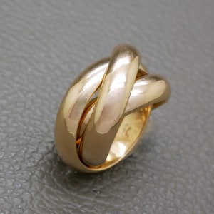 May include: A polished gold ring featuring a design of three interlocking bands that overlap to create a continuous, rounded shape. The metal surface is smooth and reflective, showcasing a warm, metallic yellow tone throughout the piece.