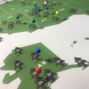 May include: A green map of the United States with push pins marking different locations. The map is labeled "National Parks". The state of Alaska is highlighted with a blue, red, and green push pin.