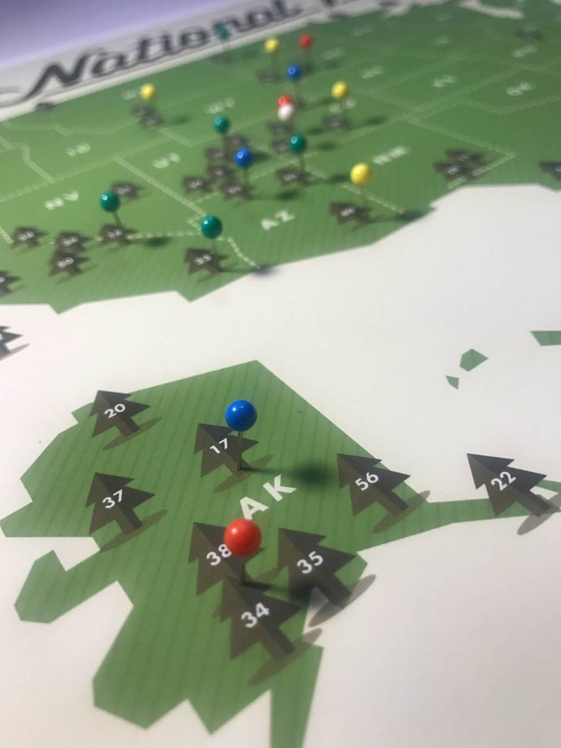 May include: A green map of the United States with push pins marking different locations. The map is labeled "National Parks". The state of Alaska is highlighted with a blue, red, and green push pin.