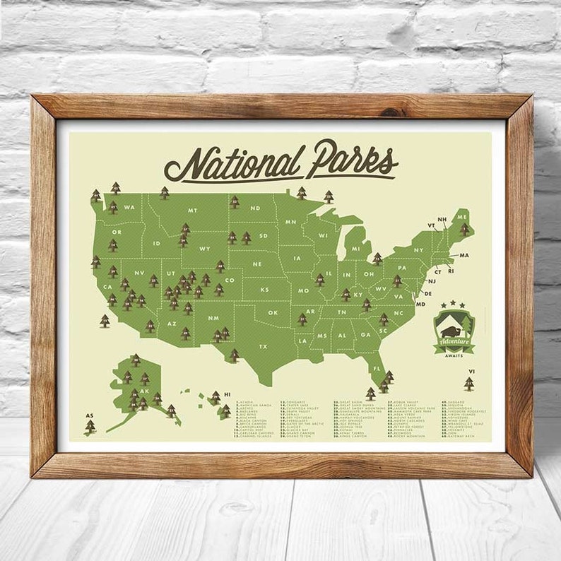 May include: A map of the United States with green pine tree icons marking the locations of all 63 National Parks. The map is framed in a brown wood frame. The text "National Parks" is written in a vintage style font at the top of the map. The text "Adventure Awaits" is written in a smaller font at the bottom of the map.