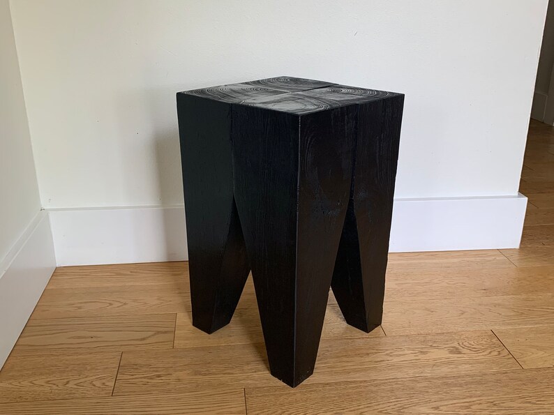 May include: A black wooden stool with a square top and four legs that are angled inwards. The stool is made of solid wood and has a natural finish.