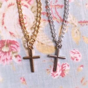 May include: Two delicate gold and silver chains with cross pendants. The chains are on a floral patterned background.