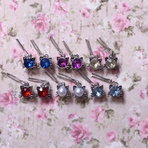 Puede incluir: Un conjunto de 10 pinzas para el pelo de plata en forma de gato con diferentes colores de piedras de imitación. Las piedras de imitación son rojas, azules, rosas, amarillas, blancas y azul claro.