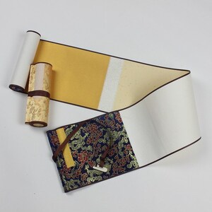 May include: A traditional Chinese scroll with a decorative fabric cover. The scroll is made of paper and has a brown wooden roller. The fabric cover is blue with gold and red floral designs.