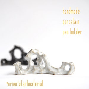 Op de afbeelding: Witte porseleinen pennenhouder in de vorm van een rotsformatie. De houder heeft een ruw, getextureerd oppervlak en is handgemaakt. "handmade porcelain pen holder" en "orientalartmaterial" staan in de afbeelding.