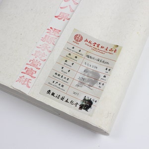 Pu&ograve; includere: Un cartoncino bianco con testo nero e un timbro rosso. Il cartoncino &egrave; etichettato "Yong Qin Tang Brand Xuan Paper Card of Product". Il testo sul cartoncino include "Name of Commodity: 精制尺八屏画纸", "Specification: 53&times;234 cm", "Quantity: 50 piece", "Weight: 2.78 kg", "Inspector Number: 01", "Date of Production: 2013 年9月4日", and "安徽泾县未乾全备级".