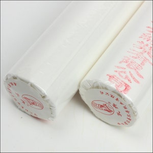 May include: Two rolls of white paper wrapped in plastic with red labels. The labels have Chinese characters and a picture of a scroll.