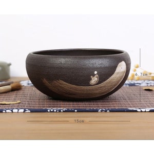 May include: A dark brown ceramic bowl with a light brown brushstroke design. The bowl is 6.7 cm tall and 15 cm wide.