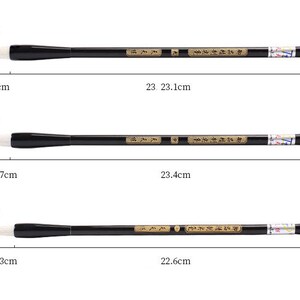 May include: Three black and white calligraphy brushes with white bristles and black handles. The brushes are 23.1 cm, 23.4 cm, and 22.6 cm long. The brush bristles are 1.1 cm, 0.9 cm, and 0.8 cm wide. The handles are 4.2 cm, 3.7 cm, and 3.3 cm long.