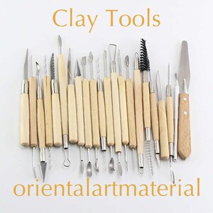 May include: A set of 25 clay sculpting tools with wooden handles. The tools have a variety of shapes and sizes for sculpting and modelling clay. The tools are arranged in a row on a white background. The text "Clay Tools" is written in gold letters above the tools. The text "orientalartmaterial" is written in gold letters below the tools.