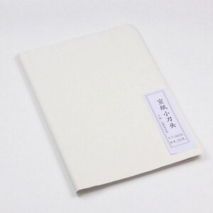 May include: A white, blank, paper notebook with a small, rectangular label on the front. The label is white with black text that reads "宣紙 小刀 光" and has additional text in Japanese.