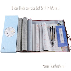 May include: A calligraphy set with a blue and white box, three black brushes, a blue and white ink stone, a white scroll with red lines, and a blue and white booklet with Chinese characters. The set is on a brown wooden surface. Water Cloth Exercise Gift Set (140x43cm)