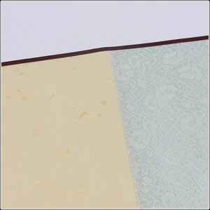 May include: A close-up of a cream-colored paper with gold flecks. The paper is attached to a light blue paper with a textured pattern.