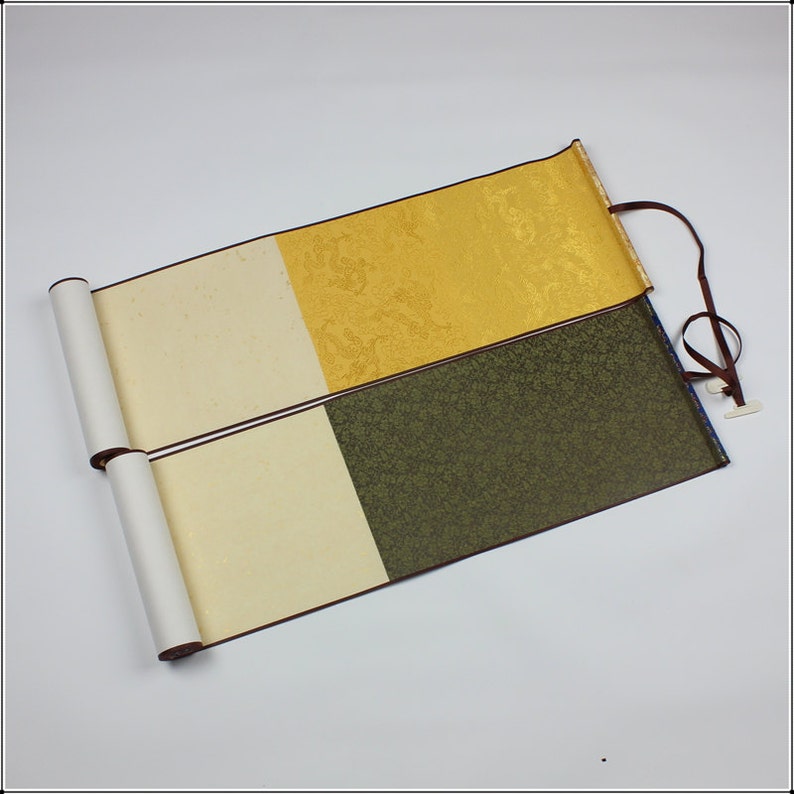 May include: Two traditional Japanese calligraphy scrolls with brown wooden dowels. The scrolls are made of white paper with a gold and green patterned fabric backing.