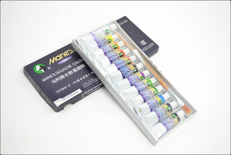 Puede incluir: Un juego de 12 pinturas gouache en tubos, con un pincel, en una caja blanca y negra. La caja dice "Marie's Gouache Colours" y "马利牌水粉画颜料" en chino. Los tubos est&aacute;n etiquetados con el nombre del color en ingl&eacute;s y chino.