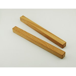 May include: Two wooden dowels, one slightly longer than the other, are shown against a white background. The dowels are light brown in colour and have a smooth, polished finish.
