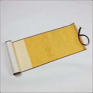 May include: A traditional Japanese scroll with a gold background and intricate patterns. The scroll is rolled up and tied with a brown ribbon.