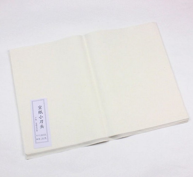 May include: A white, blank, paper notebook with a small, white label on the front cover. The label has Japanese text that reads "Washi 小刀尖".