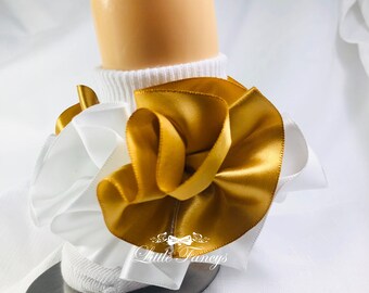 May include: White baby socks with a gold satin bow and white ruffle trim. The socks are on a silver plate and the text "Little Fancys" is visible on the socks.