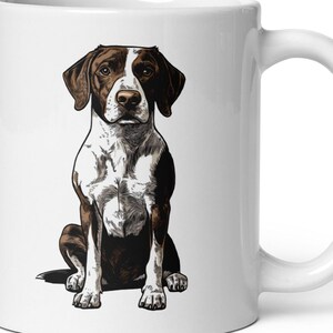 May include: White ceramic mug featuring a detailed illustration of a seated dog. The dog has brown and white markings, with brown ears and a white chest. The mug has a curved handle and a glossy finish.
