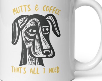 May include: White ceramic coffee mug with a black and white illustration of a dog's face and the text "MUTTS & COFFEE THAT'S ALL I NEED" in yellow.