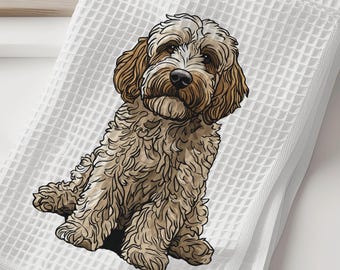 May include: White waffle-weave kitchen towel featuring a detailed illustration of a Cockapoo dog. The dog has brown and cream-colored fur and is sitting on the folded towel. The towel is on a white surface.