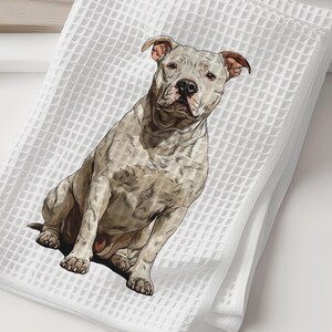 May include: White waffle-weave towel featuring a detailed illustration of a seated pit bull. The dog is depicted in shades of gray and tan, with a focused expression. The towel is folded and stacked.