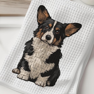 May include: White waffle-weave kitchen towel featuring a detailed illustration of a Pembroke Welsh Corgi dog. The dog has black, white, and brown fur. The towel is folded and sits on a white surface.
