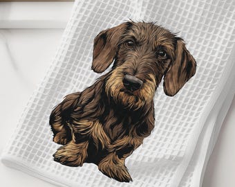 May include: A white waffle-weave kitchen towel featuring a detailed illustration of a brown and tan wire-haired dachshund. The dog is depicted in a seated position with its head tilted slightly, showcasing its textured fur and long floppy ears.