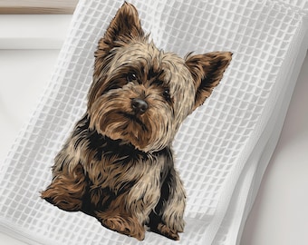 May include: White waffle-weave towel featuring a detailed illustration of a Yorkshire Terrier dog. The dog has brown and black fur and is centered on the folded towel. The towel is on a white surface.