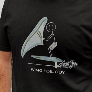 May include: A black t-shirt with a stick figure illustration of a person wing foiling. The text "WING FOIL GUY" is printed below the illustration.