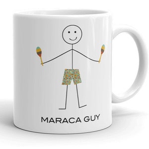 May include: White ceramic mug with a black stick figure holding two maracas. The stick figure is wearing patterned shorts. The text "MARACA GUY" is printed on the bottom of the mug.