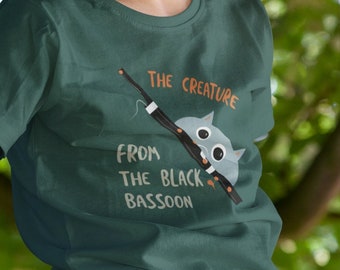 May include: A young person wearing a green t-shirt with a cartoon creature and the text "The Creature from the Black Bassoon".