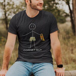 May include: A dark blue t-shirt with a stick figure illustration of a person holding a cornet. The text "Cornet Guy" is printed below the illustration.