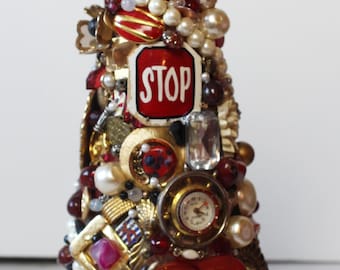 May include: A red, white, and gold Christmas tree ornament made of various trinkets, including a red stop sign, a clock face, and a red heart. The tree is topped with a red star.