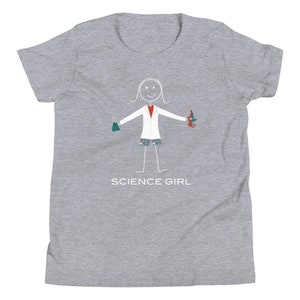 Puede incluir: Camiseta gris para j&oacute;venes con una ilustraci&oacute;n de un personaje de palo que lleva una bata de laboratorio blanca, sosteniendo un vaso de precipitados y un microscopio. El texto "SCIENCE GIRL" est&aacute; impreso debajo de la ilustraci&oacute;n.
