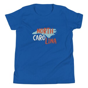 May include: A royal blue youth t-shirt with a white outline of the state of North Carolina and the text "NORTH CAROLINA" in red and white lettering.