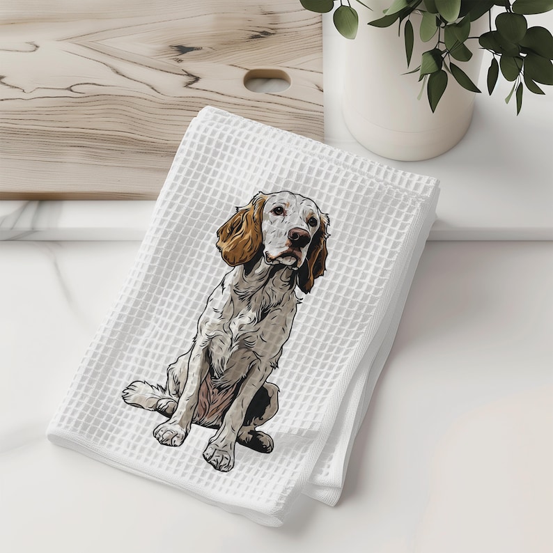 May include: White waffle-weave kitchen towel featuring a detailed illustration of a dog. The dog has brown and white fur, with floppy ears and a focused expression. The towel is folded and sits on a white surface, suggesting a home decor or pet-themed product.